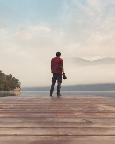 Landscape photographer at lake pier in misty morning